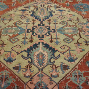 Traditional geometric rug with a sage green central medallion and stylized patterns on a terracotta red field.