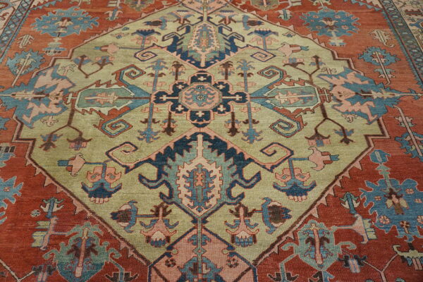 Traditional geometric rug with a sage green central medallion and stylized patterns on a terracotta red field.