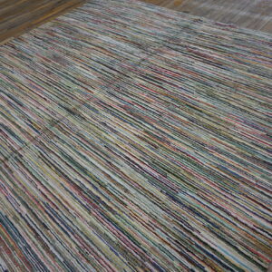 A multicolored striped rug with narrow textured bands lies on dark distressed wood flooring.