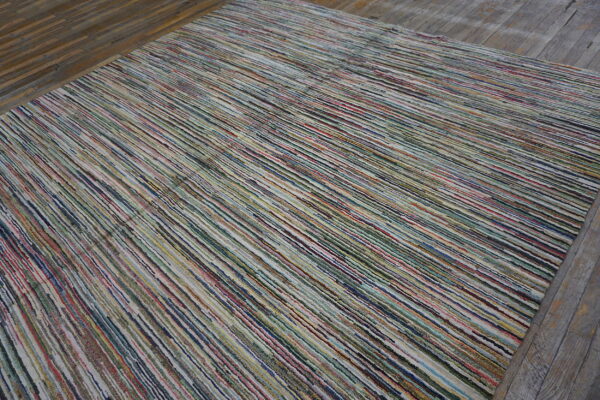A multicolored striped rug with narrow textured bands lies on dark distressed wood flooring.