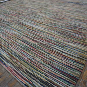 A multicolored striped rug with a low, textured pile rests on distressed wooden floorboards.
