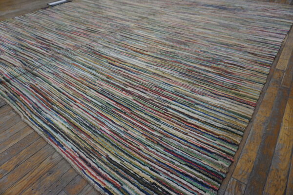 A multicolored striped rug with a low, textured pile rests on distressed wooden floorboards.
