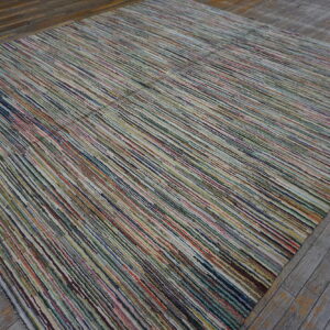 A linear-textured rug with narrow multicolored stripes rests on rustic weathered gray wood flooring.