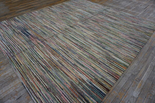 A linear-textured rug with narrow multicolored stripes rests on rustic weathered gray wood flooring.