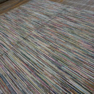 Low-pile rug with colorful, narrow vertical stripes rests on worn gray wooden floorboards.