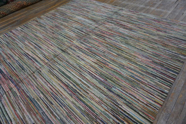 Low-pile rug with colorful, narrow vertical stripes rests on worn gray wooden floorboards.