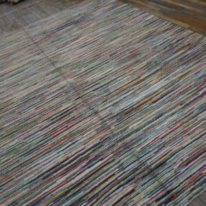 A multicolored striped rug with dense, variegated fibers lies on weathered wooden plank flooring.