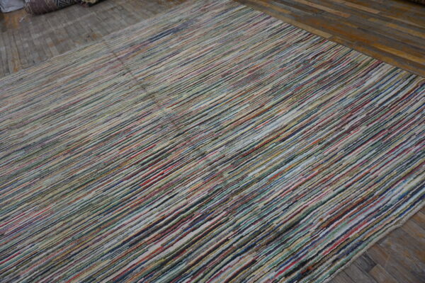 A multicolored striped rug with dense, variegated fibers lies on weathered wooden plank flooring.