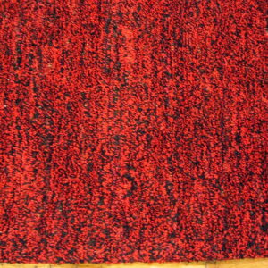 Red and black mottled, high-pile rug on light wood flooring, showing a green binding edge.