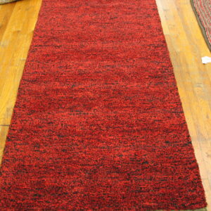 High-pile red and black speckled runner rug displayed lengthwise on golden wood plank flooring.