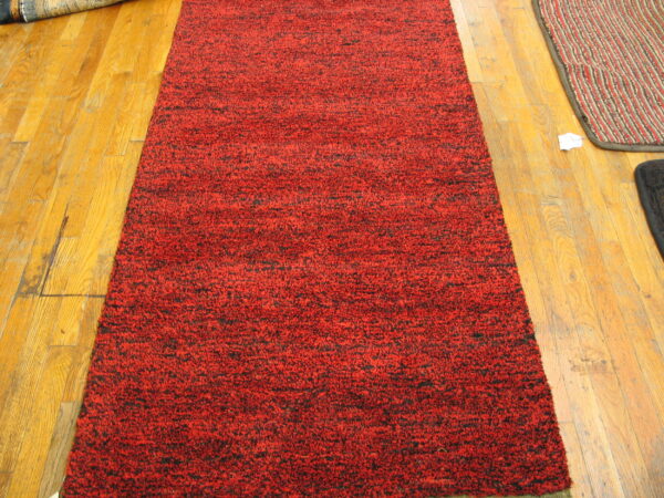High-pile red and black speckled runner rug displayed lengthwise on golden wood plank flooring.