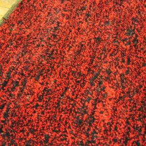 Red and black nubby pile rug texture with olive green trim visible against hardwood flooring.