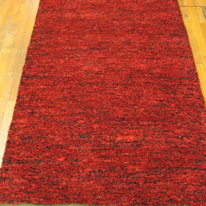 A textured runner rug in mottled red and black pile lies on honey-colored hardwood flooring.