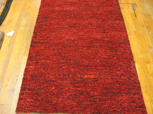 A textured runner rug in mottled red and black pile lies on honey-colored hardwood flooring.