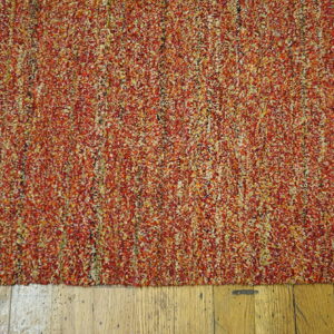 Textured rug with variegated red, orange, and yellow pile features a narrow vertical green stripe on wood.