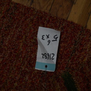 Multi-tonal, shaggy rug with red and yellow fibers rests on brown plank wood flooring.