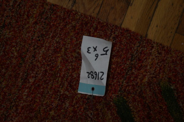 Multi-tonal, shaggy rug with red and yellow fibers rests on brown plank wood flooring.