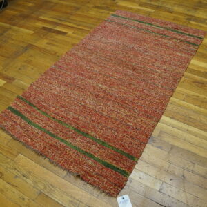 Textured red and yellow rug featuring two green stripes lies on worn, golden-toned wood floors.