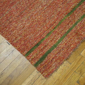 Speckled red and orange textured rug featuring two dark green stripes on worn hardwood flooring.