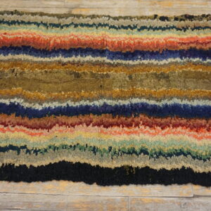 A multicolored shag rug with wide, irregular horizontal stripes rests on light, rustic wood flooring.