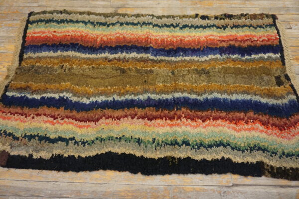 A multicolored shag rug with wide, irregular horizontal stripes rests on light, rustic wood flooring.