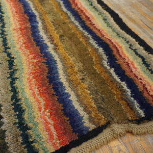 Shaggy, multicolored striped rug with uneven lines of red, olive, blue, and gold on wood flooring.