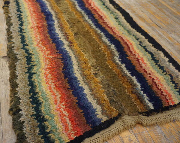Shaggy, multicolored striped rug with uneven lines of red, olive, blue, and gold on wood flooring.