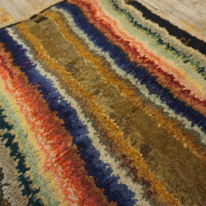 Textured rug with thick, wavy stripes in blue, orange, brown, and green on light wood floors.