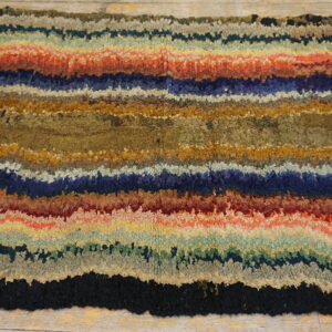High-pile rug with jagged horizontal stripes of blue, red, gold, olive, and brown on rustic wood flooring.