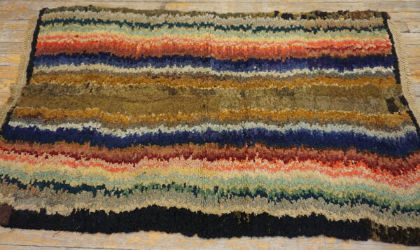 High-pile rug with jagged horizontal stripes of blue, red, gold, olive, and brown on rustic wood flooring.