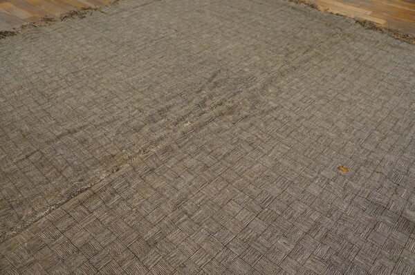 Brown flatwoven rug with a detailed basketweave texture resting on dark hardwood flooring.