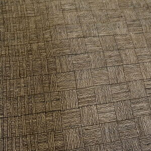Textured dark brown and tan checkerboard rug with visible fringe lying on a wood surface.