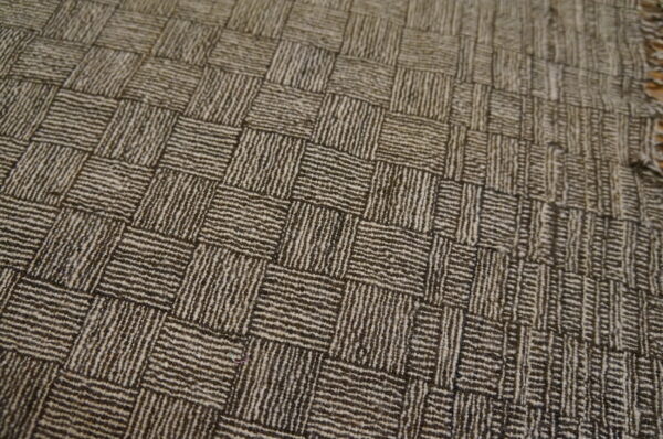 Close-up view of a low-pile rug showing a striped, two-tone brown basketweave design and fringed edge.