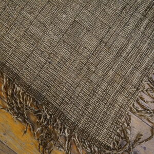 Brown and tan flatweave rug with a woven checkerboard pattern and shaggy fringe resting on a wood floor.