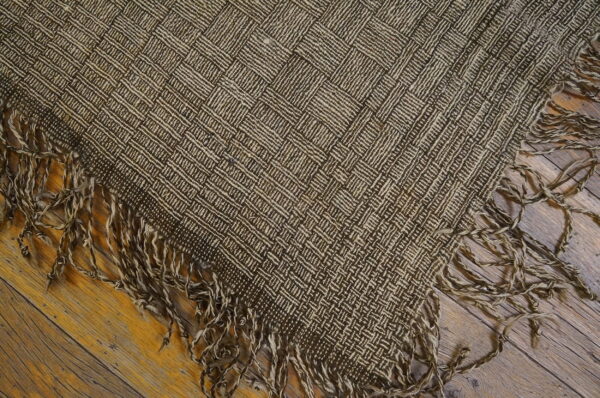 Brown and tan flatweave rug with a woven checkerboard pattern and shaggy fringe resting on a wood floor.