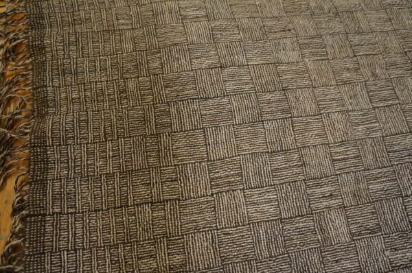 Textured brown and beige rug with a square grid pattern rests on a wooden floor.