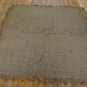 Worn green-brown flatweave rug with a checkerboard pattern and fringe rests on distressed wooden planks.