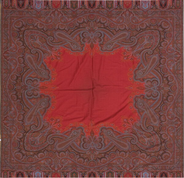 Square red textile with a wide, complex border featuring intricate paisley motifs in browns and blues.