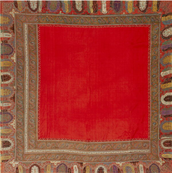 A vibrant red rug with elaborate, multicolored paisley and shield-like decorative borders.