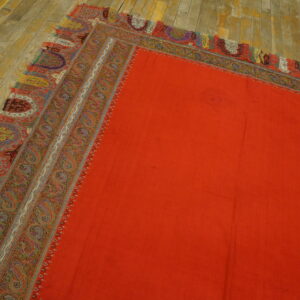 Solid orange rug field detailed with a complex paisley border resting on a distressed wood floor.
