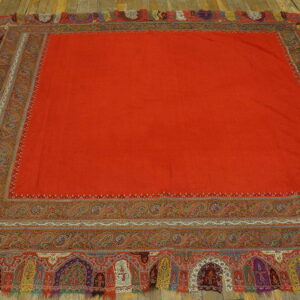 Square red flatweave textile rug with detailed multicolored paisley and arched borders on wood flooring.