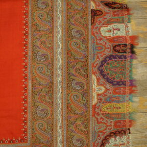 Red ground with multicolored bands of detailed paisley and stylized borders over light wood.