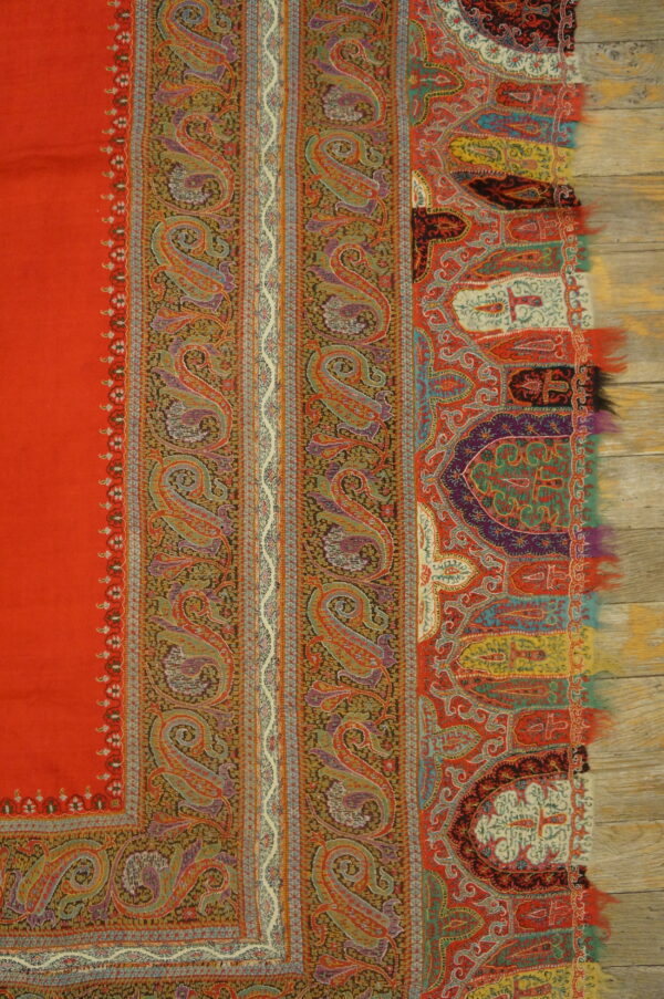 Red ground with multicolored bands of detailed paisley and stylized borders over light wood.