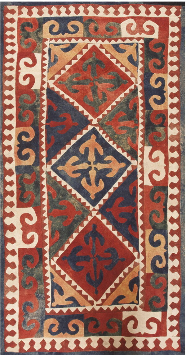 Red, navy, tan, and olive rug featuring geometric diamonds, stylized figures, and large scrolling borders.