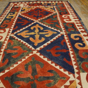 A geometric rug featuring rust, navy, gold, and cream diamonds rests on worn, light-colored wood floor planks.