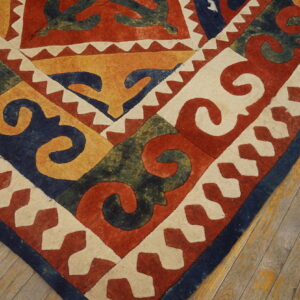 Zero-pile rug corner featuring bold scroll patterns in red, navy, yellow, green, and cream on wood flooring.