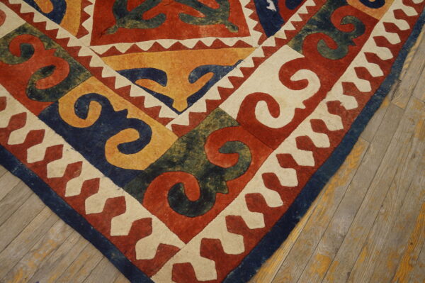 Zero-pile rug corner featuring bold scroll patterns in red, navy, yellow, green, and cream on wood flooring.