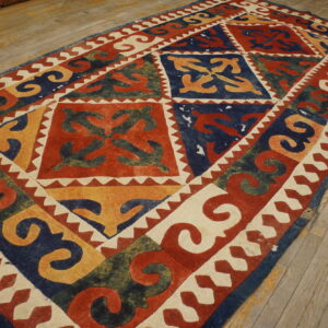 Red, blue, yellow, and cream rug with bold geometric tribal motifs lying on light, worn wood floors.