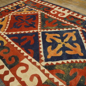 Flat rug with red, navy, gold, and off-white geometric designs featuring curving organic motifs on wood.