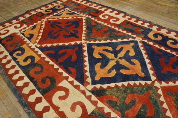 Flat rug with red, navy, gold, and off-white geometric designs featuring curving organic motifs on wood.